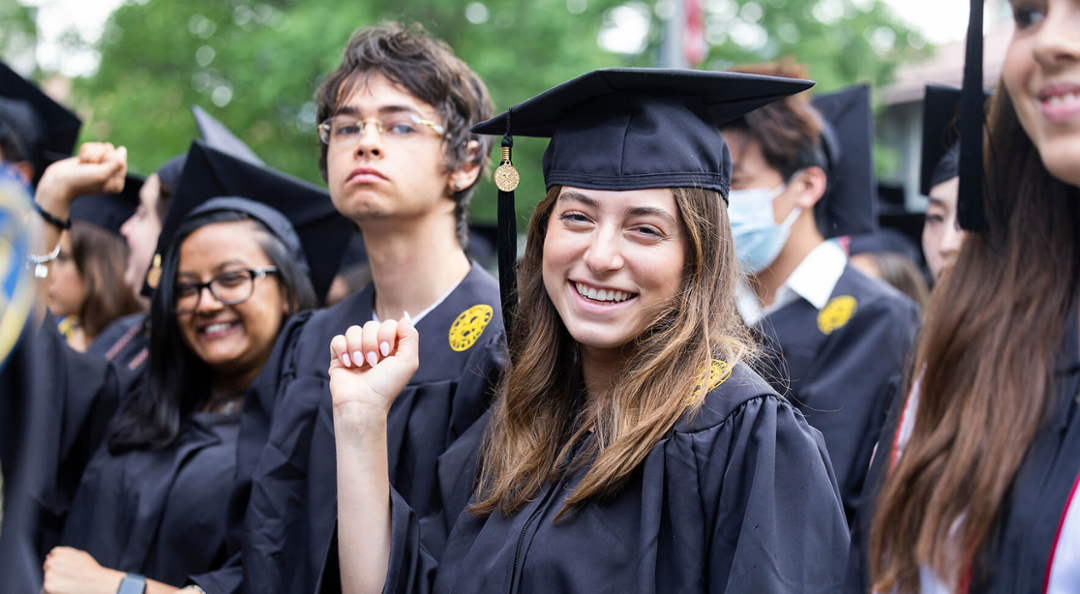 smiling student at commencement in cap and gown with other graduates