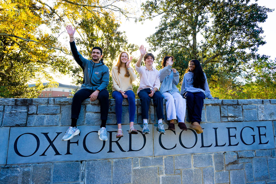 oxford college students pose on top of a stone wall that says Oxford College